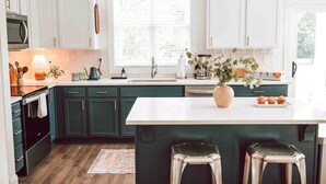 A modern kitchen with dark green cabinets, a white countertop, and a large island with stools. - Premium 3BR Home by MHM Luxury Properties (Athens)