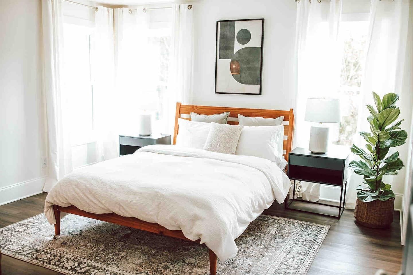 Une chambre à coucher bien rangée, avec un lit en bois, une table de chevet avec une lampe, une commode et une plante en pot.