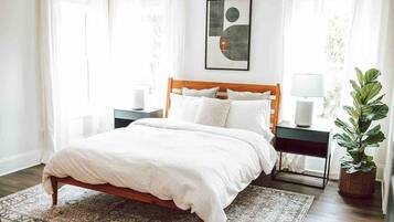 Une chambre à coucher bien rangée, avec un lit en bois, une table de chevet avec une lampe, une commode et une plante en pot.