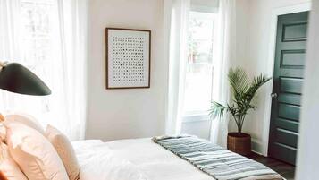 Een slaapkamer met een bed, een kunstwerk in een lijst, een kamerplant en een deur.