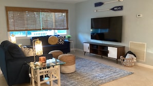 Una sala de estar con sofá, una mesa de centro, televisor y un ventanal con persianas.