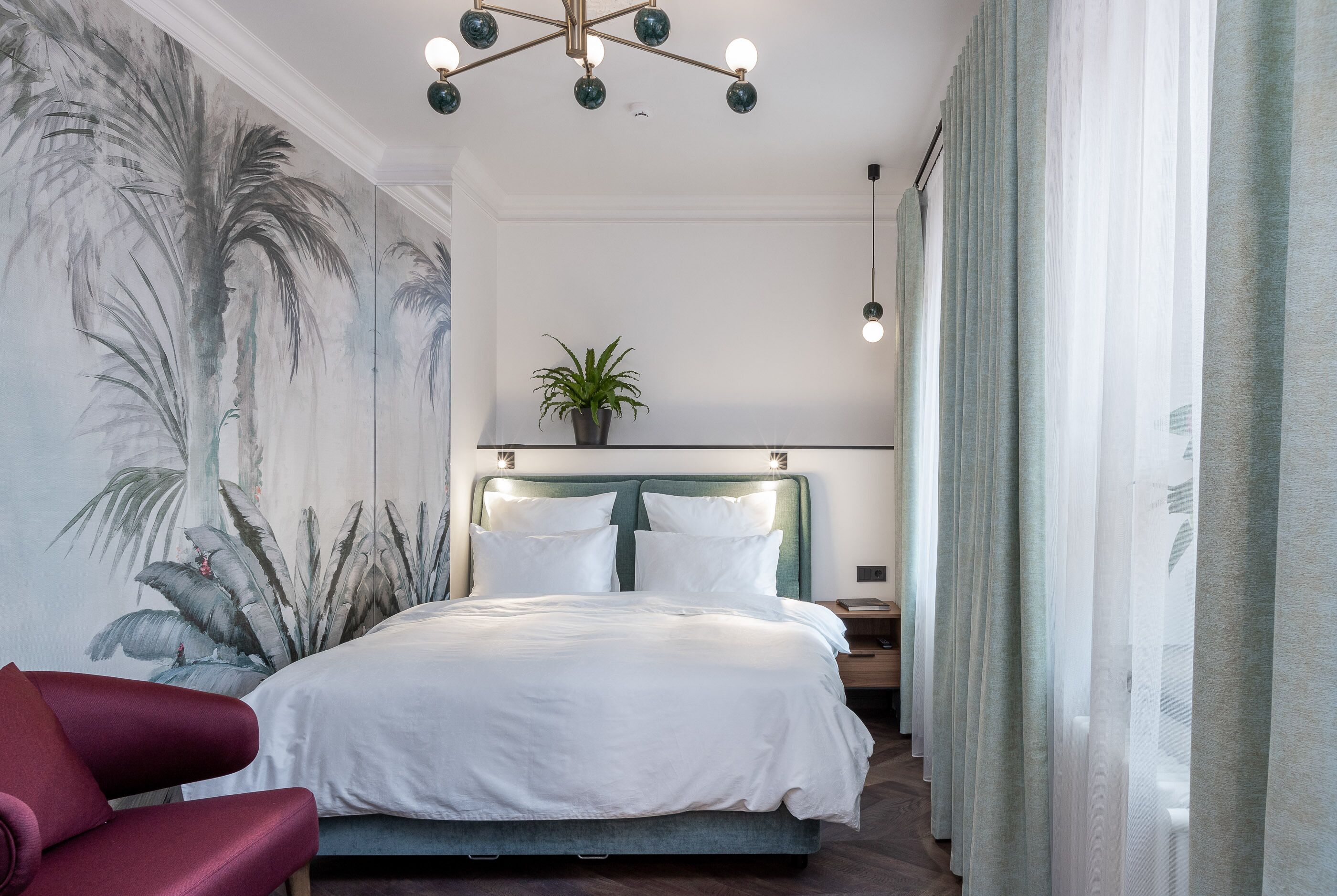 Un dormitorio con una cama grande, un cabecero con luces, una planta y una silla roja.