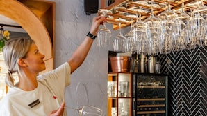 A person arranging wine glasses on a rack in a bar setting with shelves and a herringbone-patterned wall. - Zalkind Hotel Rooms&Kitchen (Minsk)