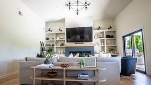 A modern living room with a large flat-screen TV, a fireplace, a sofa, and built-in shelves with decorative items. - Desert Pickle-ball Paradise in Scottsdale (Scottsdale)