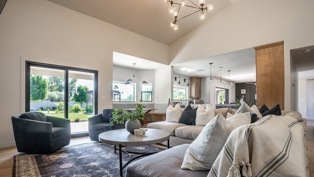 A spacious living room with a large window, a dark grey sofa, a round coffee table, and a modern chandelier. - Desert Pickle-ball Paradise in Scottsdale (Scottsdale)