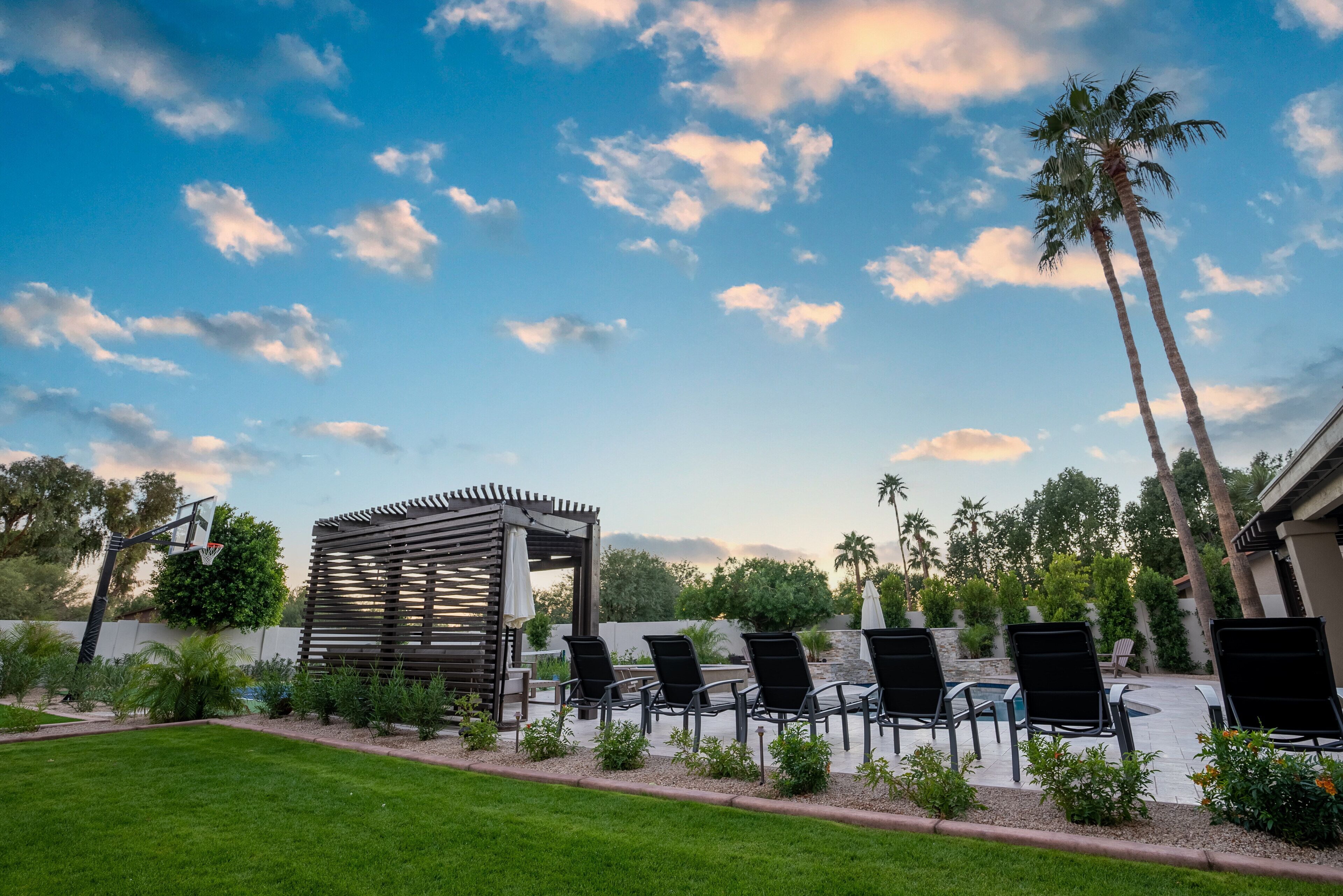 A poolside area with lounge chairs, a pergola, and palm trees.