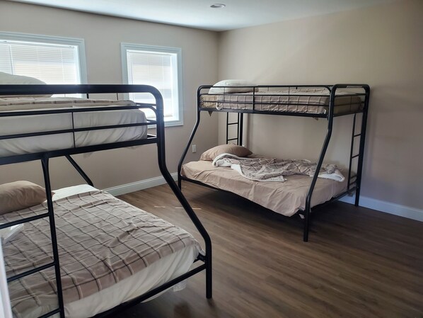 Habitación con dos literas, suelo de madera y dos ventanas con persianas.