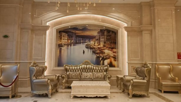 A luxurious lobby with ornate furniture, a large mural of a cityscape, and a chandelier.
