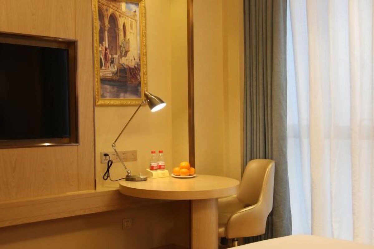 A hotel room with a round table, a single chair, a painting on the wall, and a window with curtains.