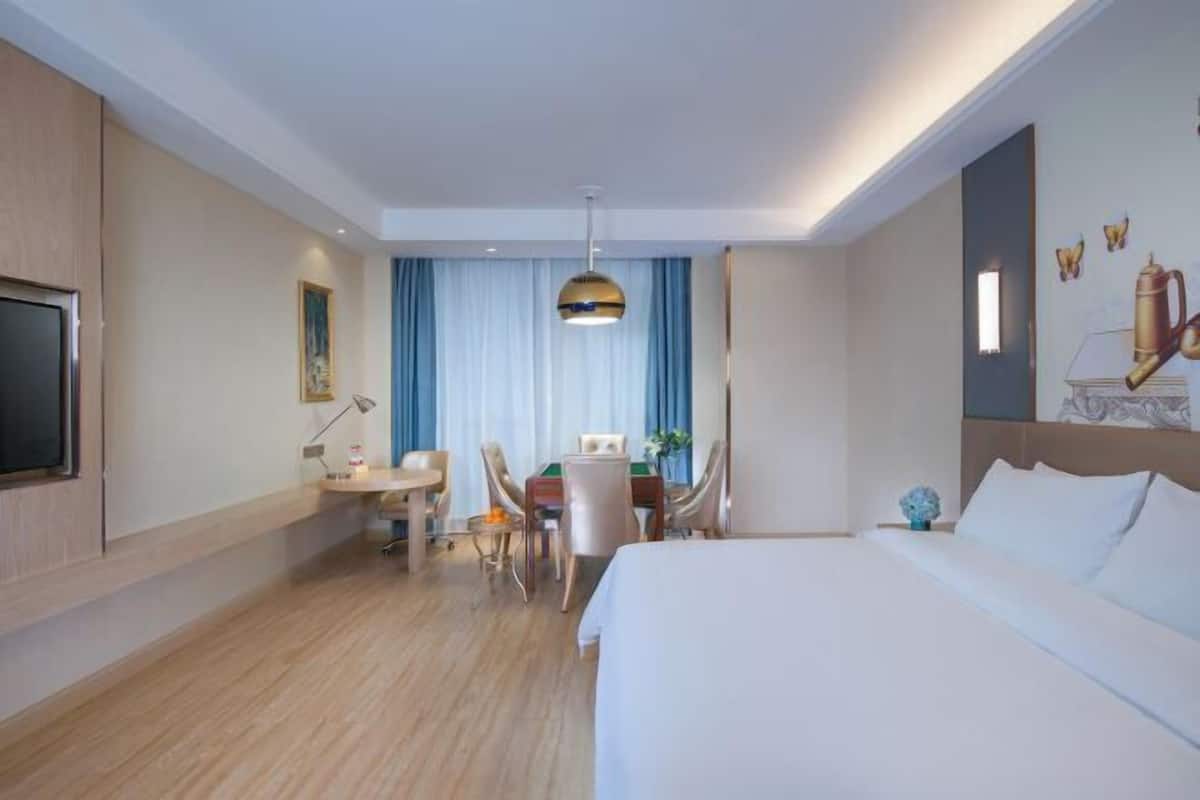 A hotel room with a large bed, a desk with chairs, a television, and a dining area with a table and chairs.