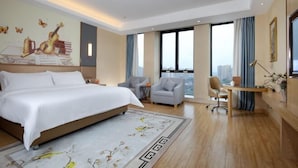 A modern hotel room with a large bed, a desk, two chairs, and a view of the city.