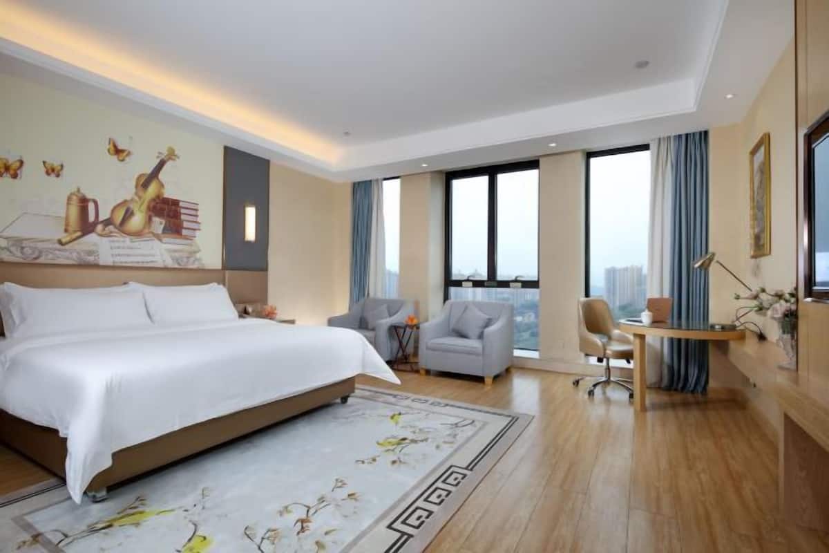 A modern hotel room with a large bed, a desk, two chairs, and a view of the city.