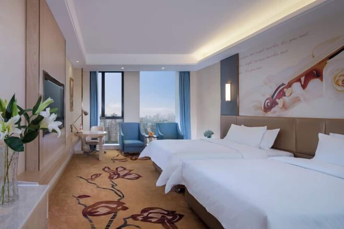 A hotel room with two beds, a desk, a chair, a large window, and a decorative wall.