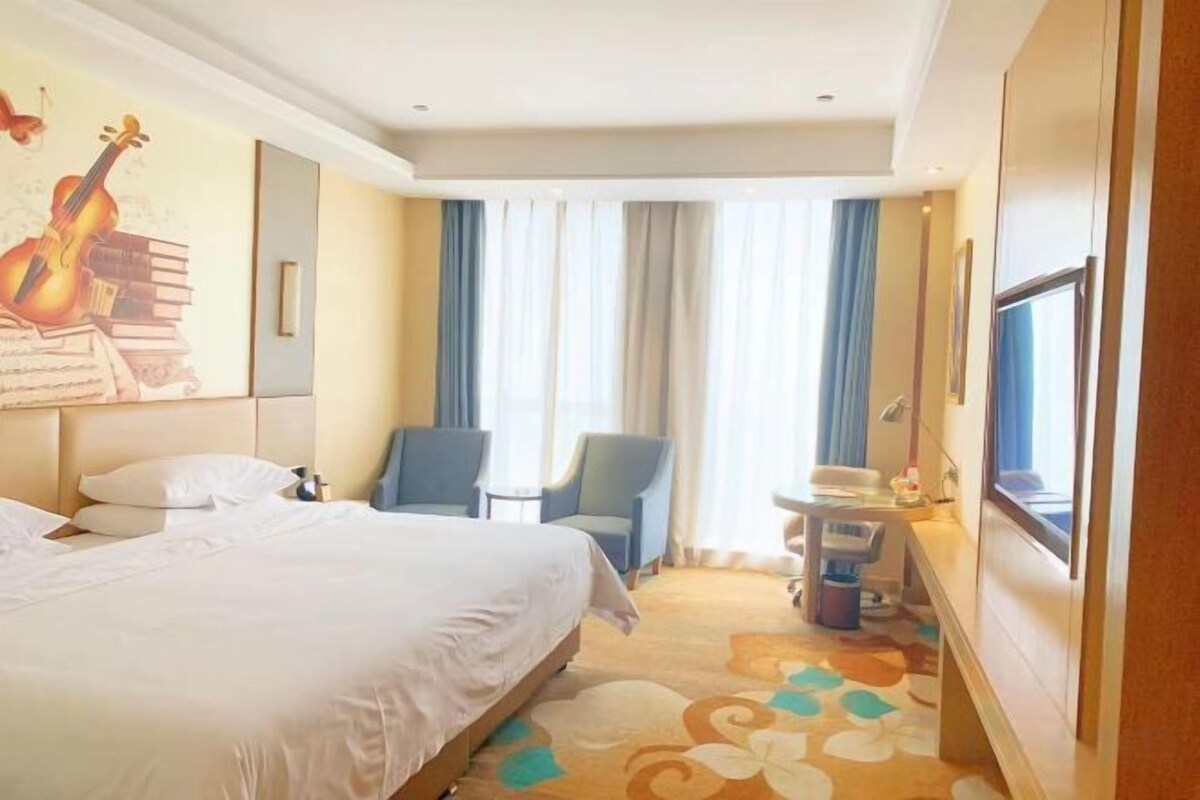 A hotel room with a bed, a desk, a chair, and a window.