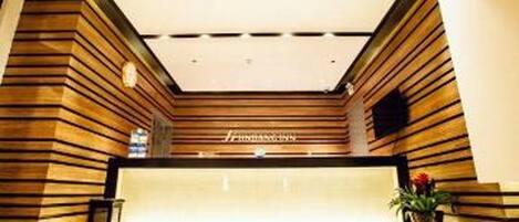 A reception area with a wooden reception desk, a potted plant, and a ceiling with recessed lighting.