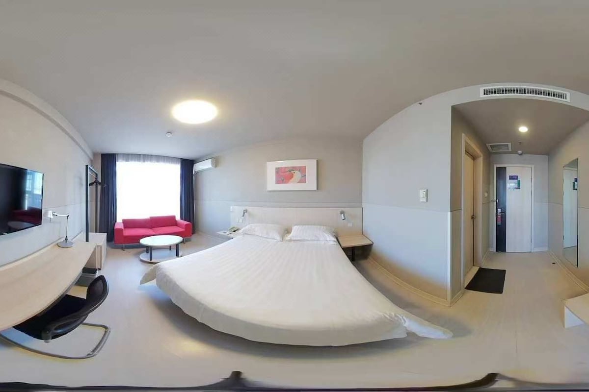 A modern hotel room with a bed, a TV, a red sofa, and a small table.
