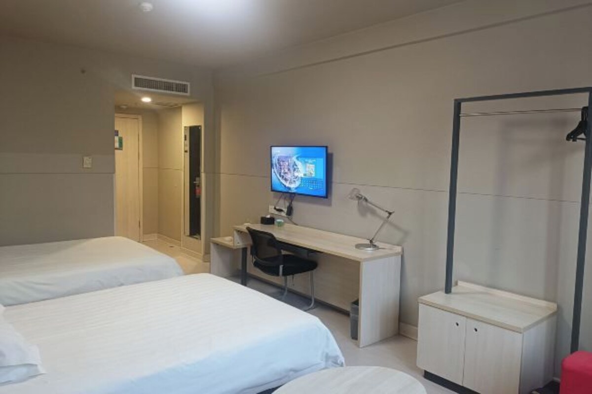 A hotel room with two beds, a desk with a chair, a television, and a shower area.