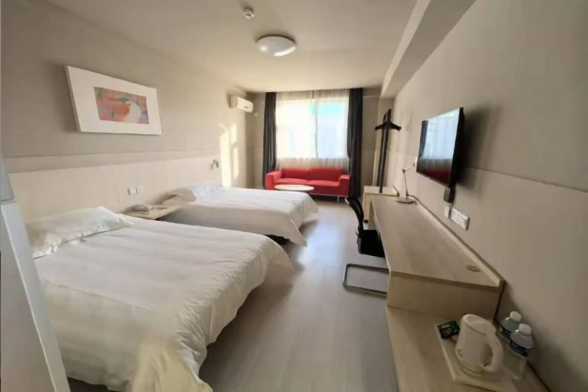 Una habitación de hotel con dos camas, un televisor, un escritorio y un sofá rojo al fondo.