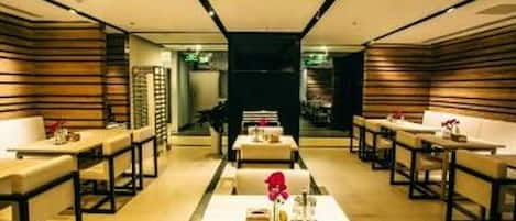 A modern interior with a central dining table, seating on both sides, and a dark-toned wall at the back.
