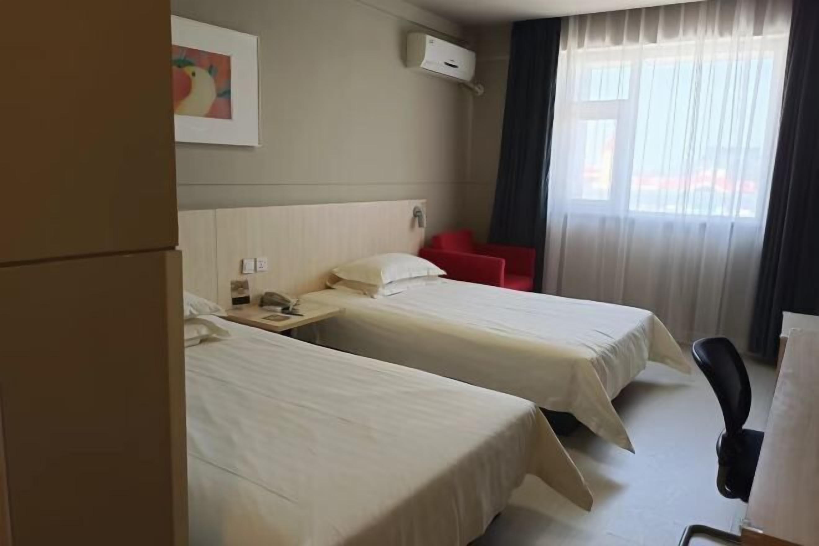 Habitación de hotel con dos camas, un escritorio, una silla, una ventana con cortinas y aire acondicionado instalado en la pared.