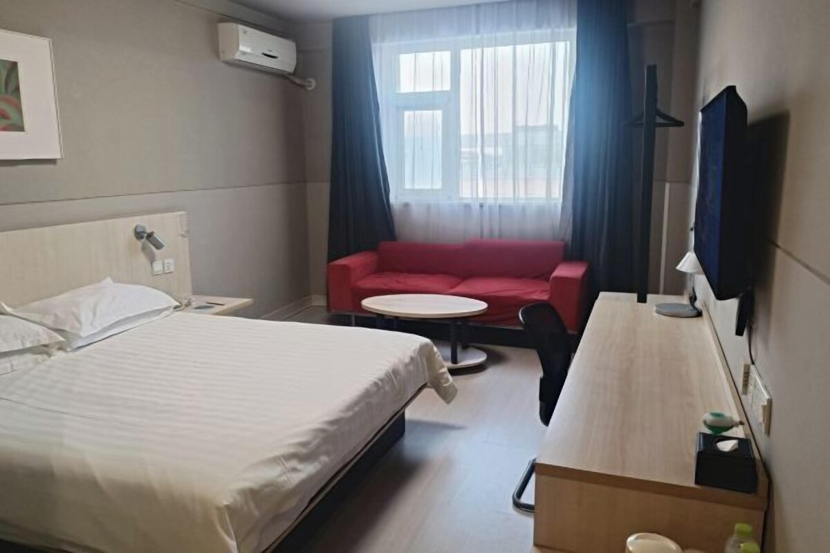 A hotel room with a bed, a red sofa, a small round table, and a TV mounted on the wall.