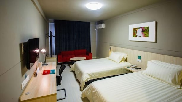 A hotel room with two beds, a desk with a lamp, a red sofa, a small round table, and a picture on the wall.