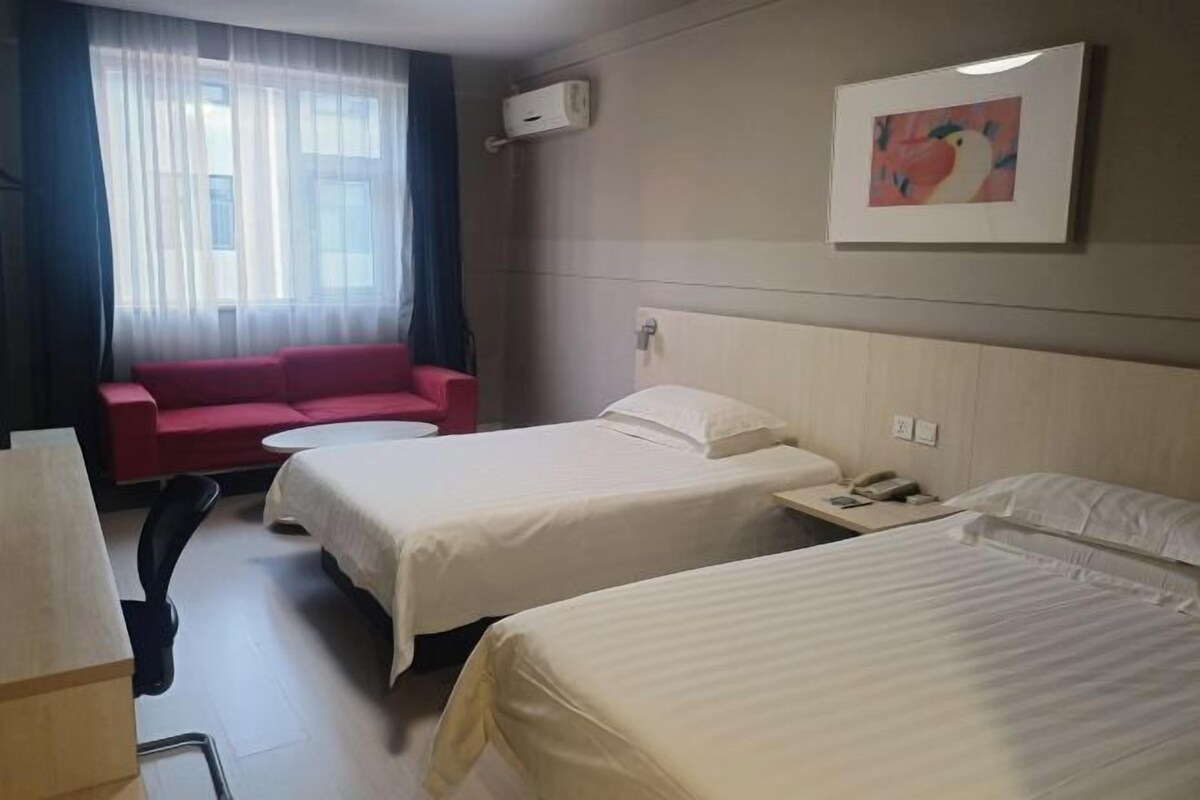 A hotel room with two beds, a red sofa, a small table, and a window with curtains.