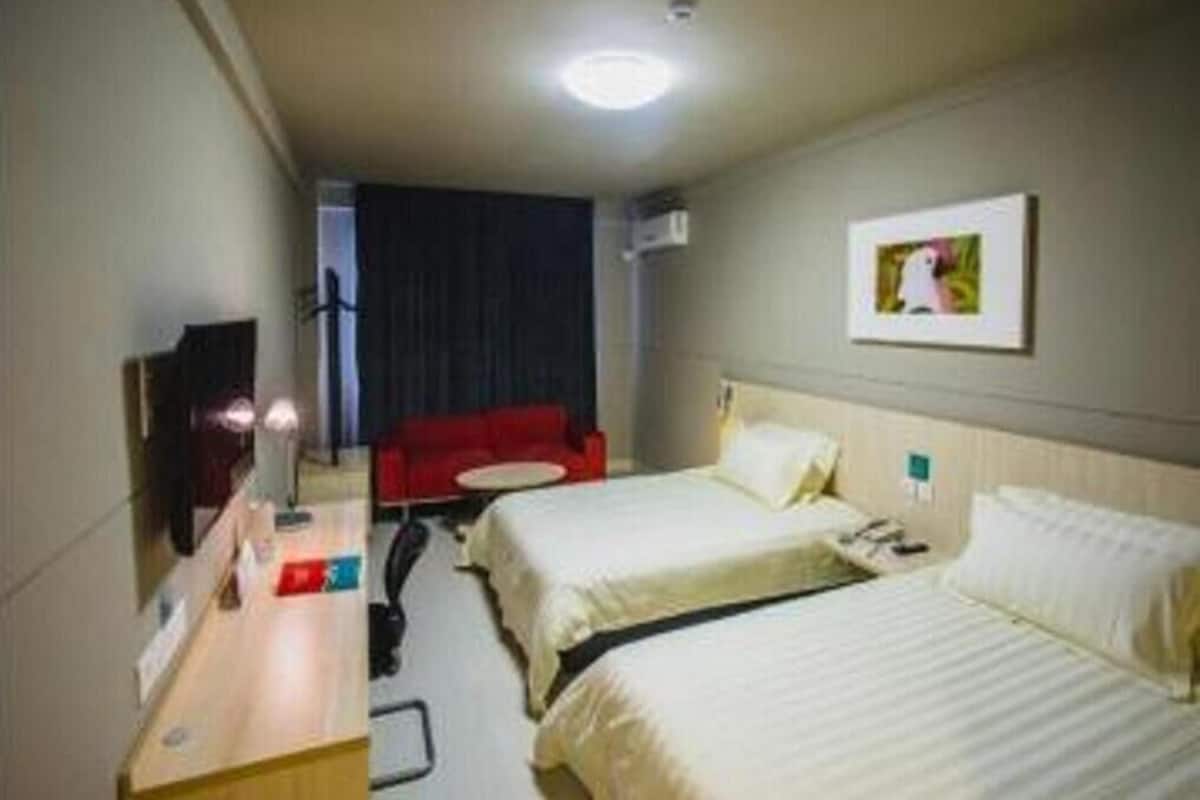 Habitación de hotel con dos camas, un escritorio con silla, un televisor y una silla roja.