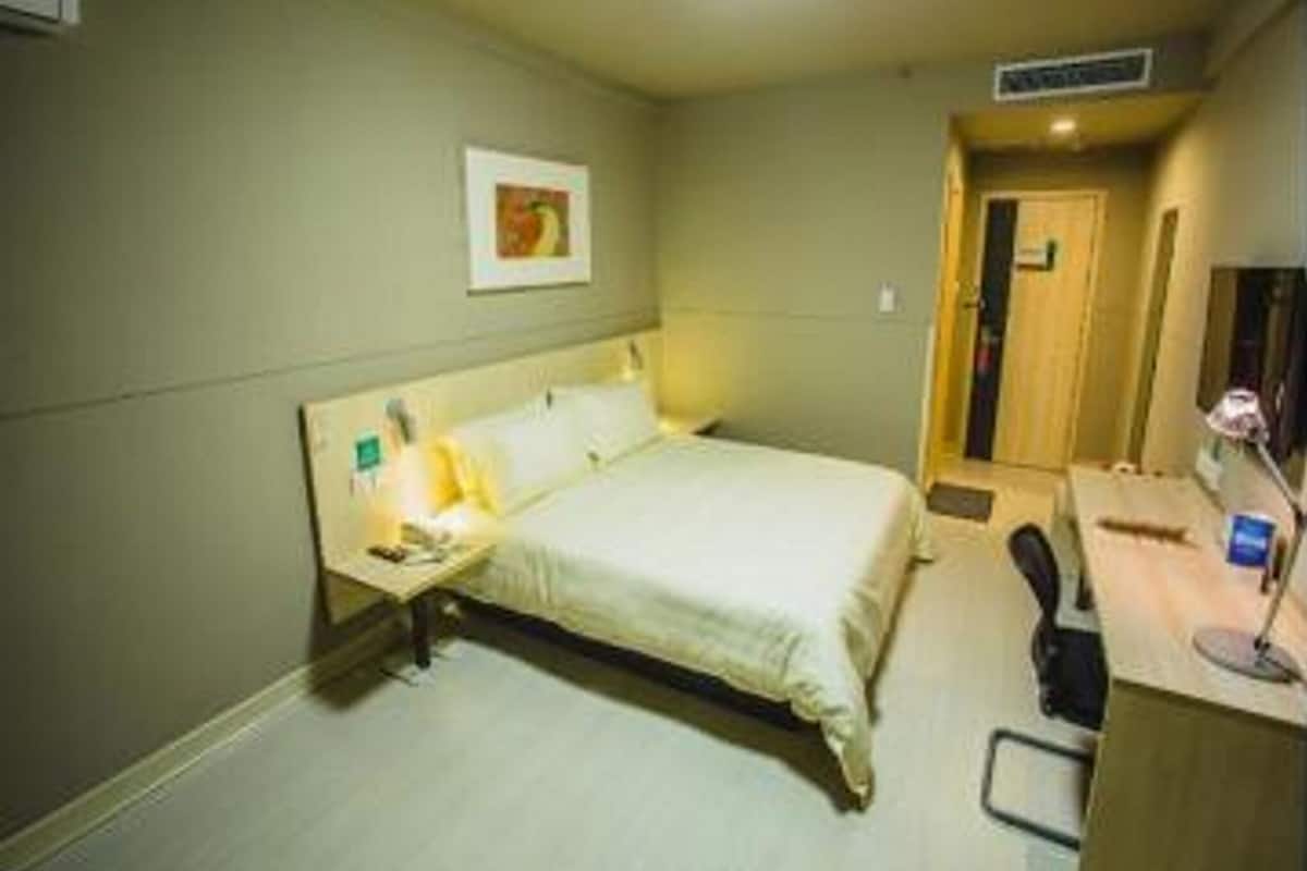 Una habitación de hotel con cama, mesita de noche, lámpara, escritorio, silla y un cuadro en la pared.