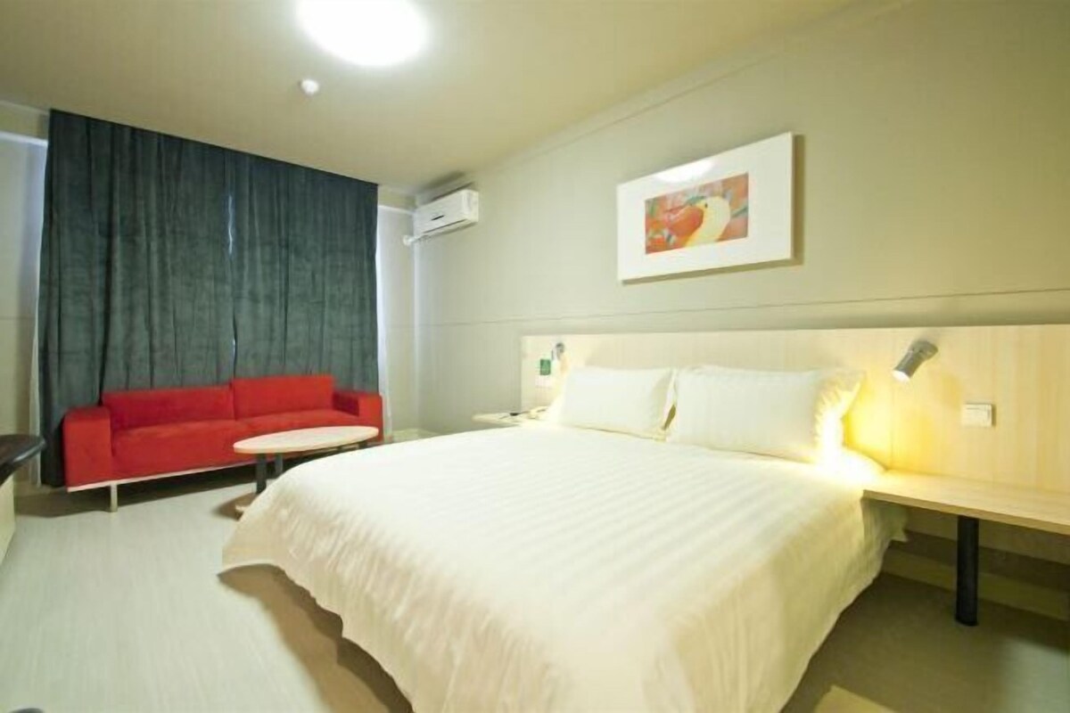 A hotel room with a bed, a red sofa, a small table, and a wall-mounted lamp.