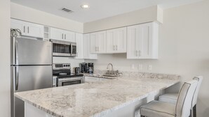A modern kitchen with white cabinetry, stainless steel appliances, and a marble countertop. - Windancer 307. Gulf Front Condo, Free Beach Service, Heated Pool, Grill. (Miramar Beach)