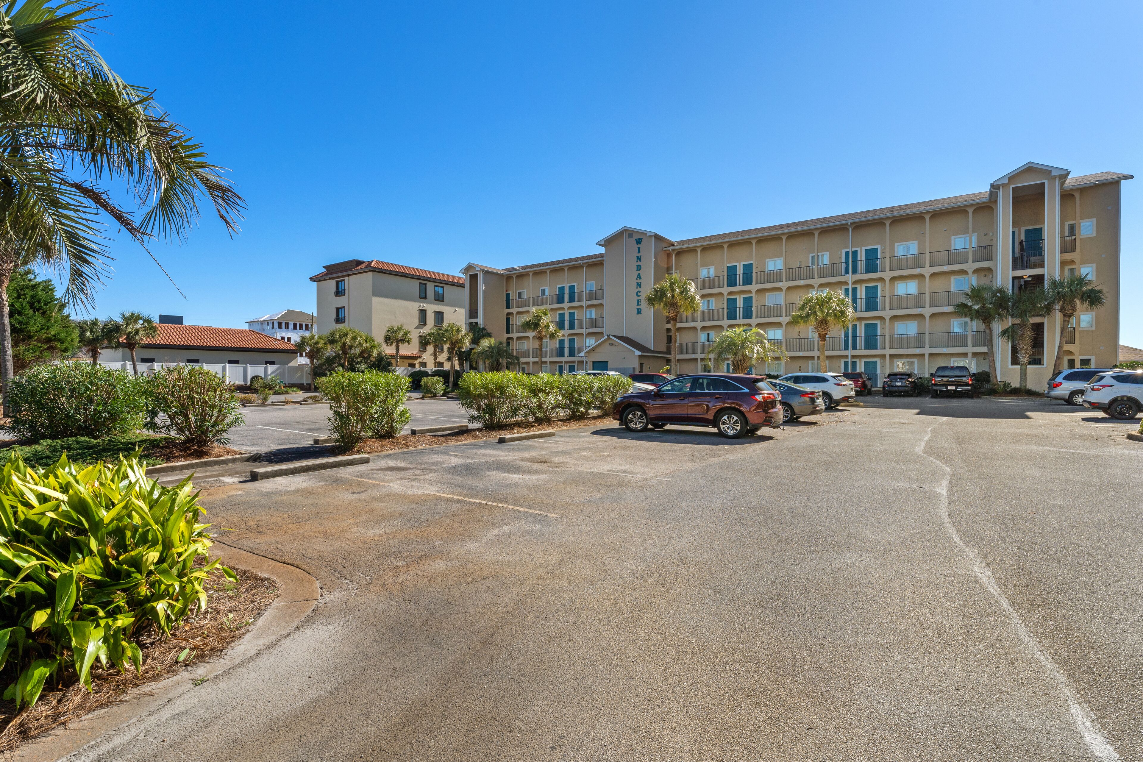 A hotel with multiple floors, a parking lot, and palm trees.
