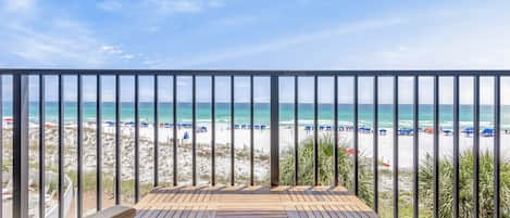 A wooden deck with a view of a beach with umbrellas and people.