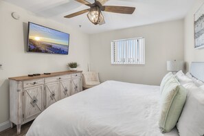 A bedroom with a bed, a ceiling fan, a TV mounted on the wall, a window with blinds, and a bedside table with a lamp. - Windancer 307. Gulf Front Condo, Free Beach Service, Heated Pool, Grill. (Miramar Beach)