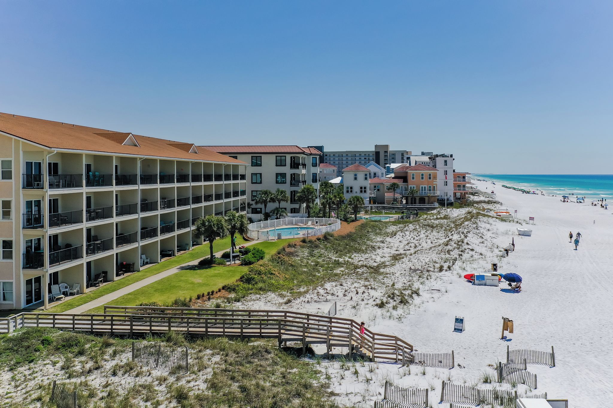 Un hotel frente a la playa con varios balcones, piscina y una playa de arena.