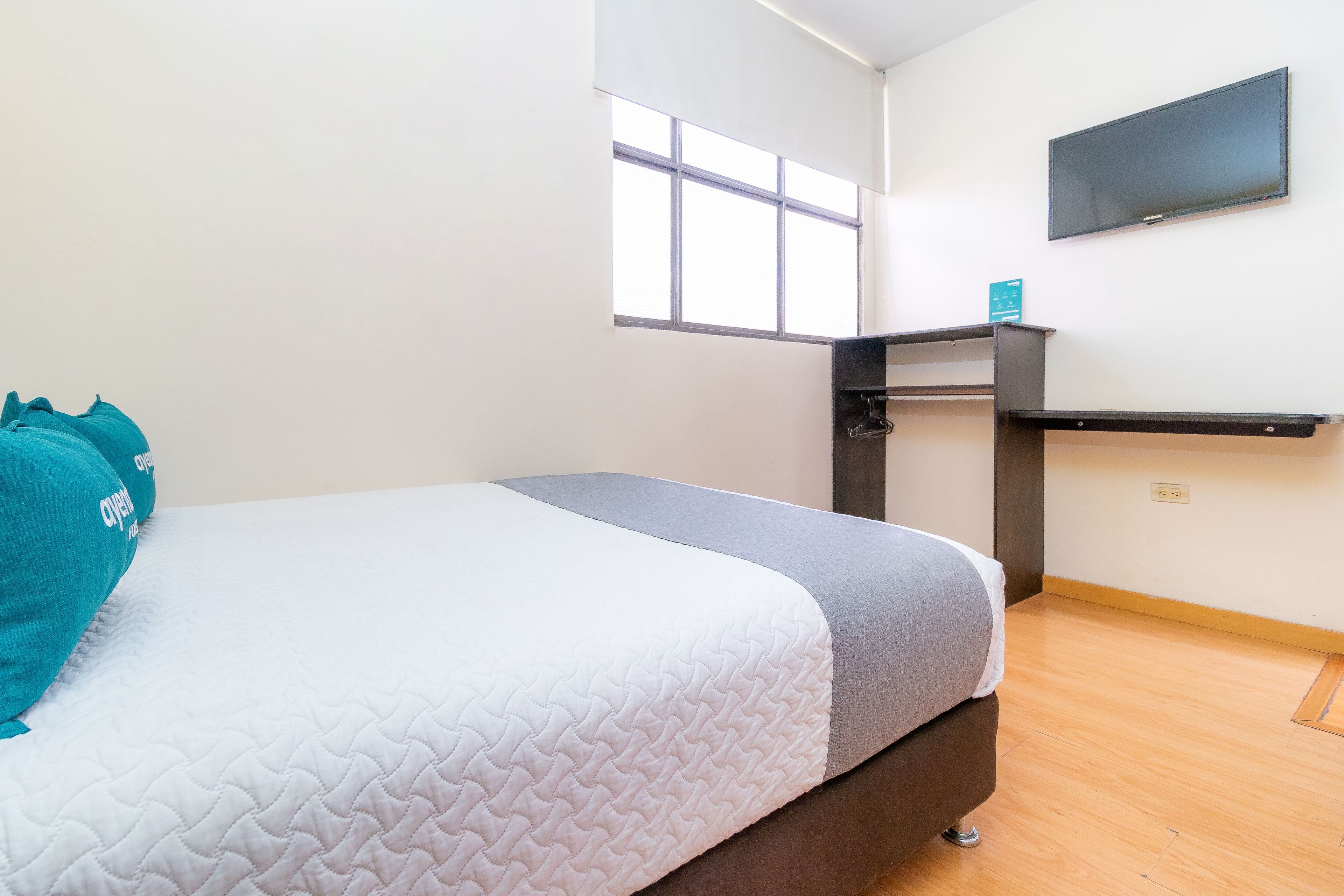 A bedroom with a bed, a desk, and a TV on the wall.