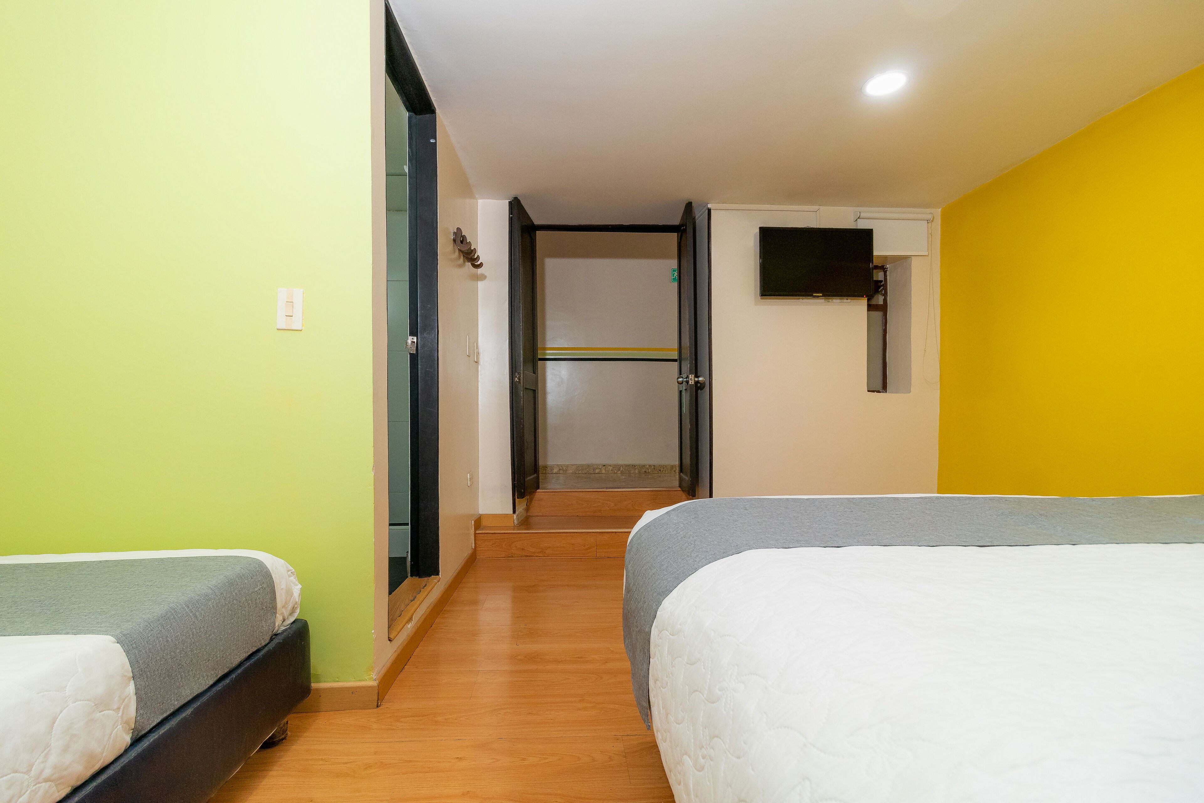 A hotel room with two beds, a television on the wall, and a staircase leading to an upper floor.