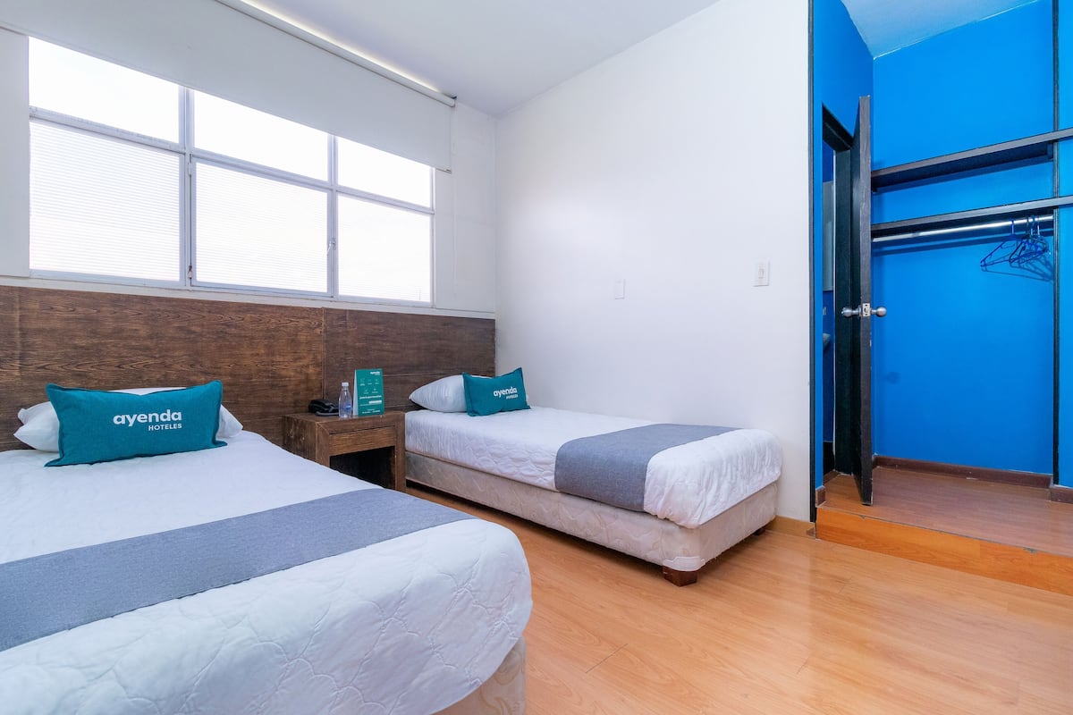 A hotel room with two beds, a wooden headboard, a blue wall, and a door leading to a bathroom.