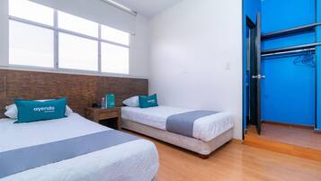Habitación de hotel con dos camas, cabecera de madera, pared azul y puerta que da a un baño.
