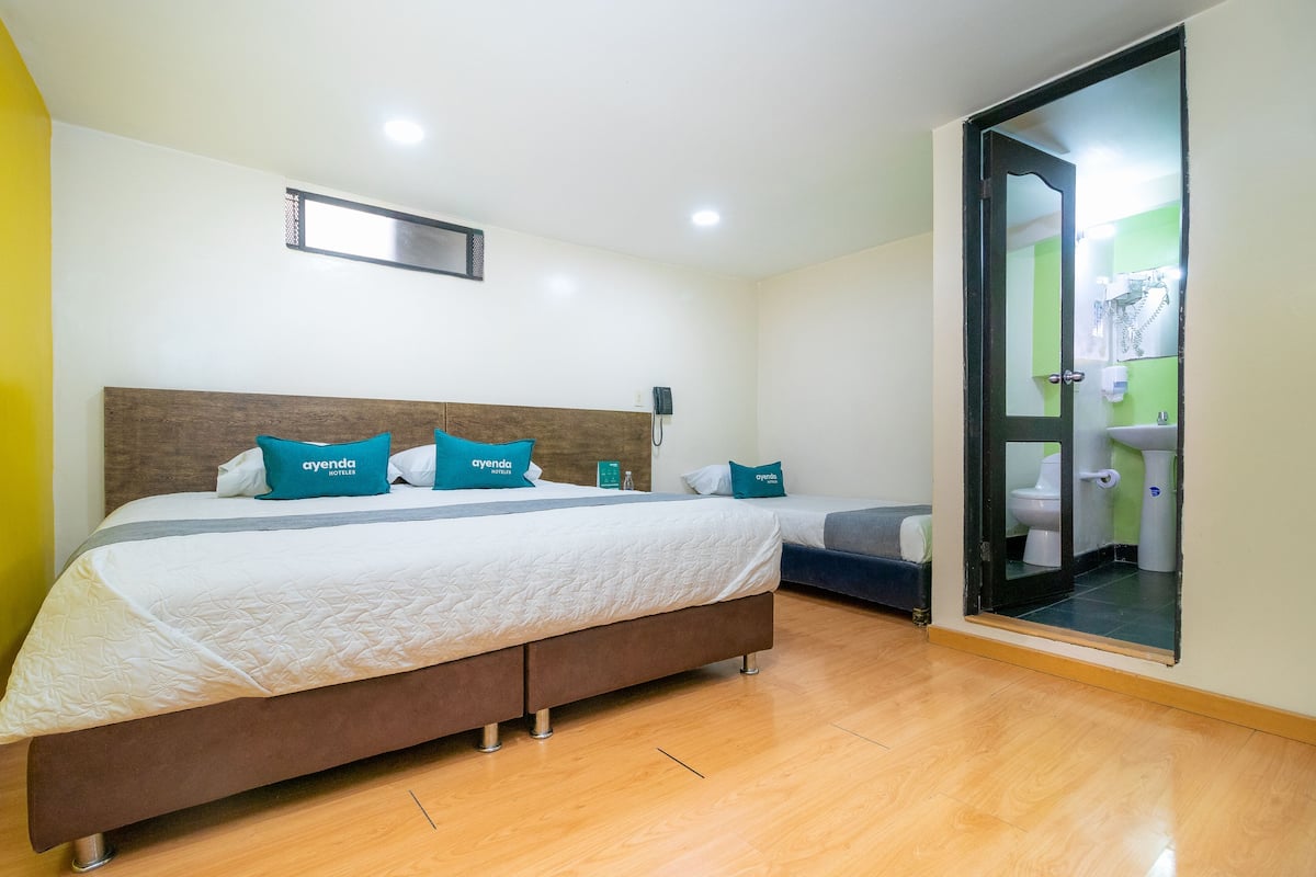 A hotel room with a large bed, a smaller bed, a wooden headboard, and a bathroom visible through a glass door.