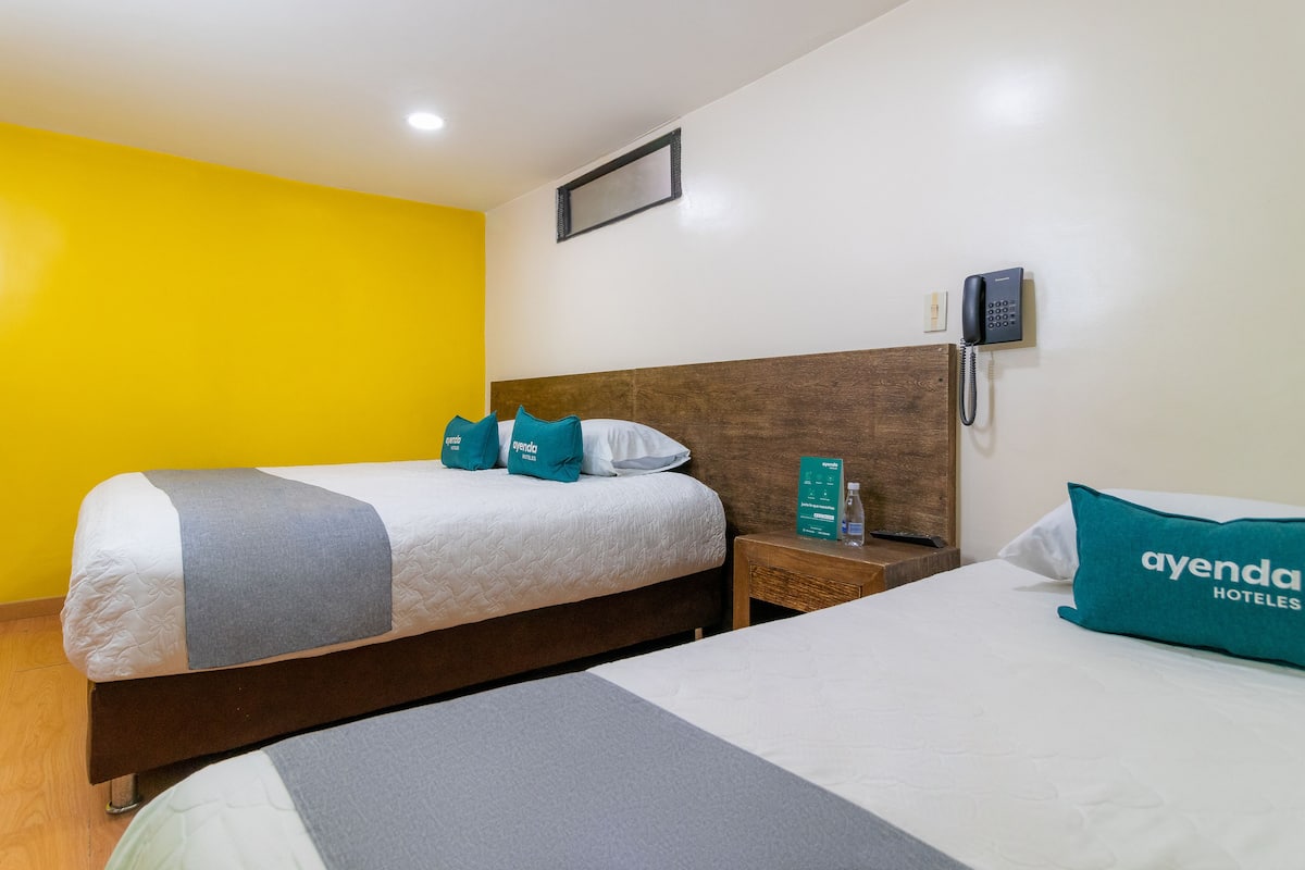 A hotel room with two beds, a wooden headboard, a bedside telephone, and a bright yellow wall.