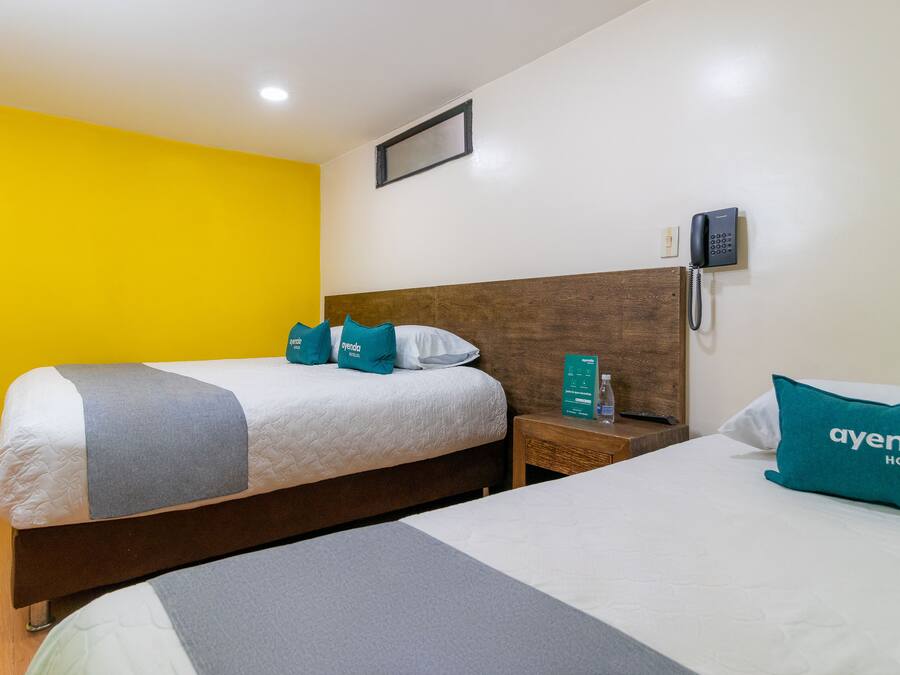 A hotel room with two beds, a wooden headboard, a bedside telephone, and a bright yellow wall.