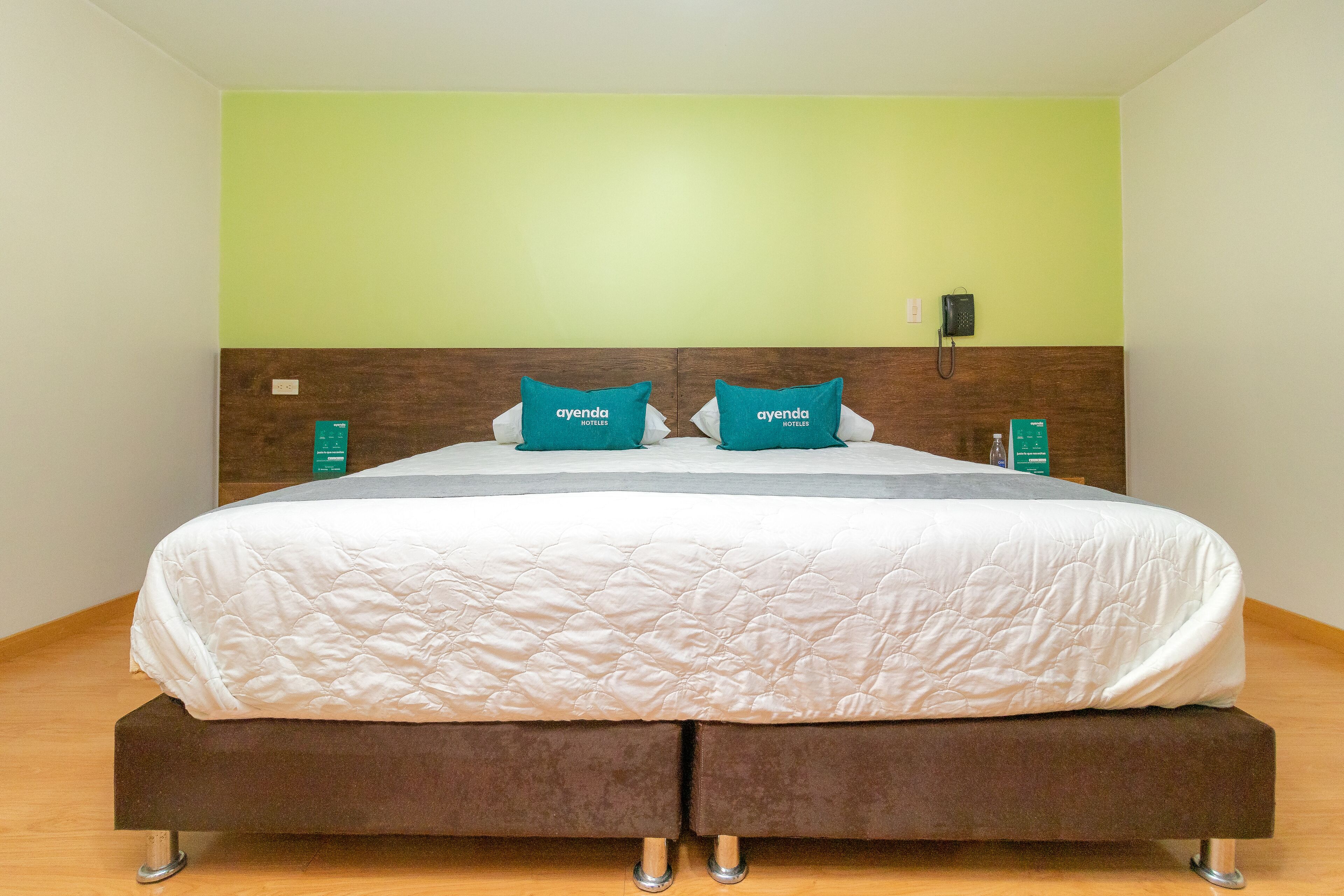 A neatly made bed with a white quilt, two teal pillows, and a brown headboard.