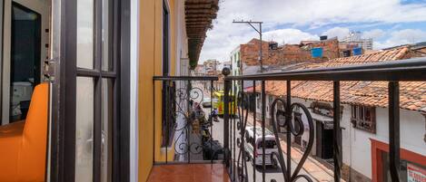 Un balcón con vistas a la calle, suelo de baldosas y barandilla de metal.