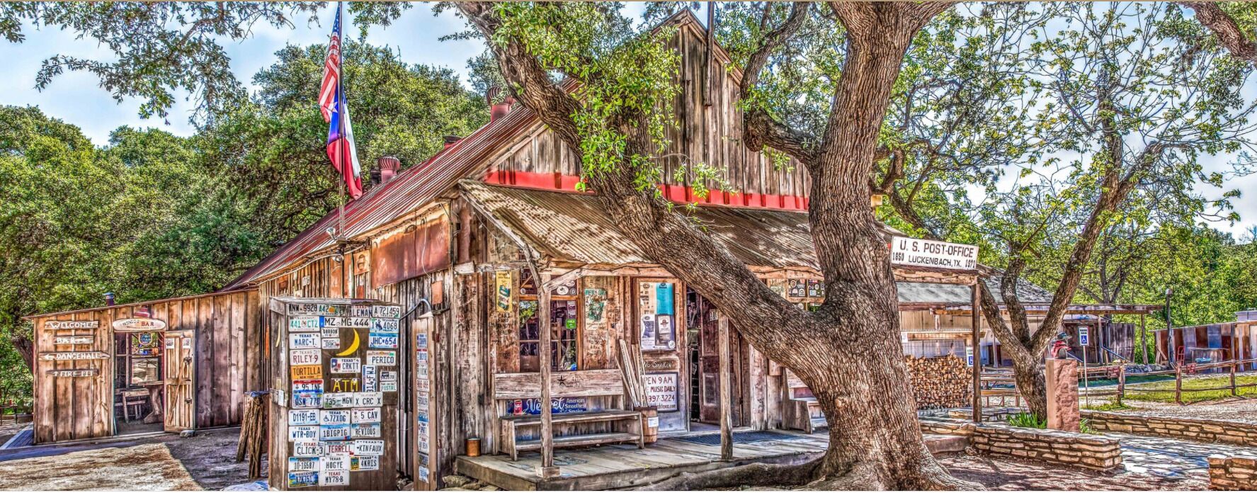 A rustic wooden building with a porch, a flag, and various signs.