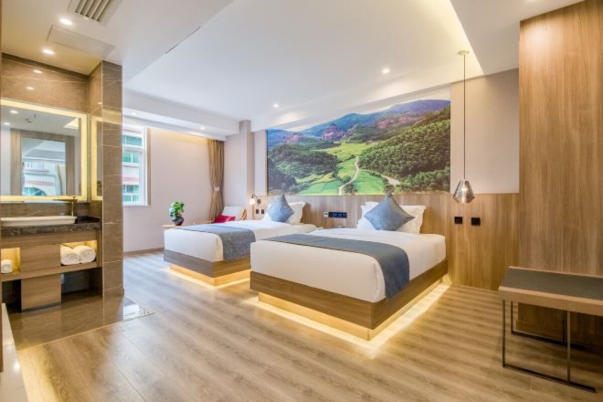 Una habitación de hotel moderna con dos camas, un cuadro de paisaje grande, un escritorio de madera y un baño con espejo y estanterías.
