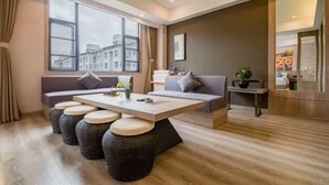 A modern living room with a sofa, a coffee table, and a view of buildings through large windows. - Manya Hotel (Xinping)
