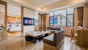 A modern hotel room with a sofa, a coffee table, a TV, and a large window offering a city view. - Manya Hotel (Xinping)