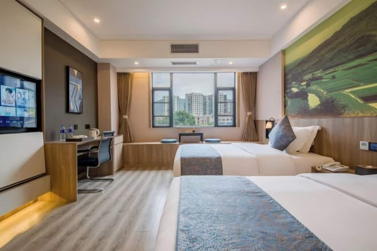Habitación de hotel con cama, escritorio, silla, televisión y una ventana grande con vistas a la ciudad.