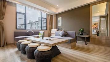 Una sala de estar moderna con un sofá, una mesa de centro y vistas a edificios a través de amplios ventanales.